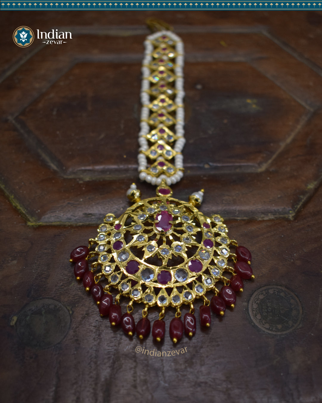 A close-up image of a Hyderabadi Jadau maang tika, adorned with dark pink and white CZ Polki stones and faux pearls. The maang tika is handcrafted with gold-plated alloy and features intricate Jadau work