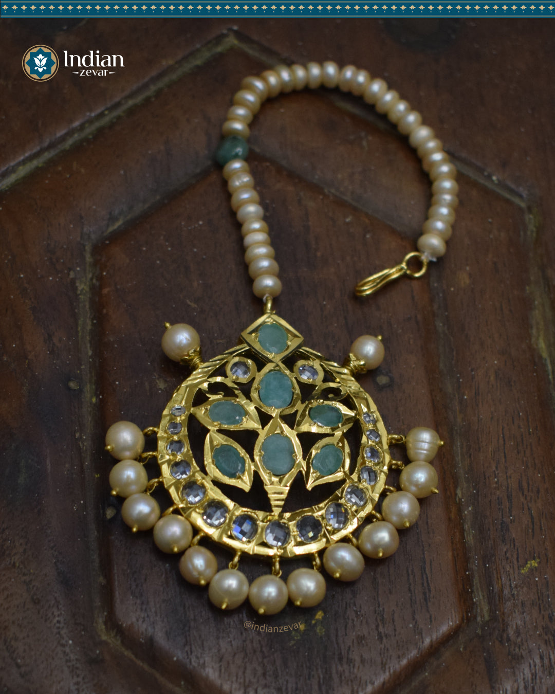 A close-up image of a Hyderabadi Jadau maang tika, adorned with emeralds, CZ Polki stones, and real freshwater pearls. The maang tika is handcrafted with gold-plated alloy and features intricate Jadau work.