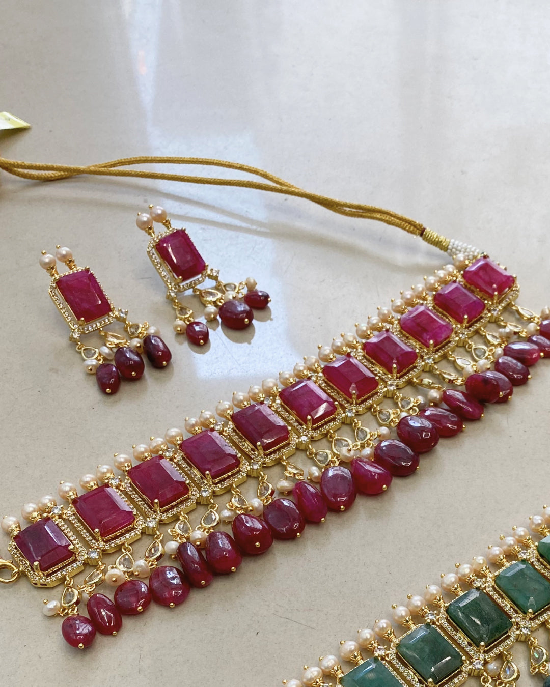 Jewelry set with red gemstones and gold accents on a light background. Handcrafted Indo-Western choker set with pearls, emerald accents & Jadau work – perfect Indian bridal jewelry and wedding choker design.