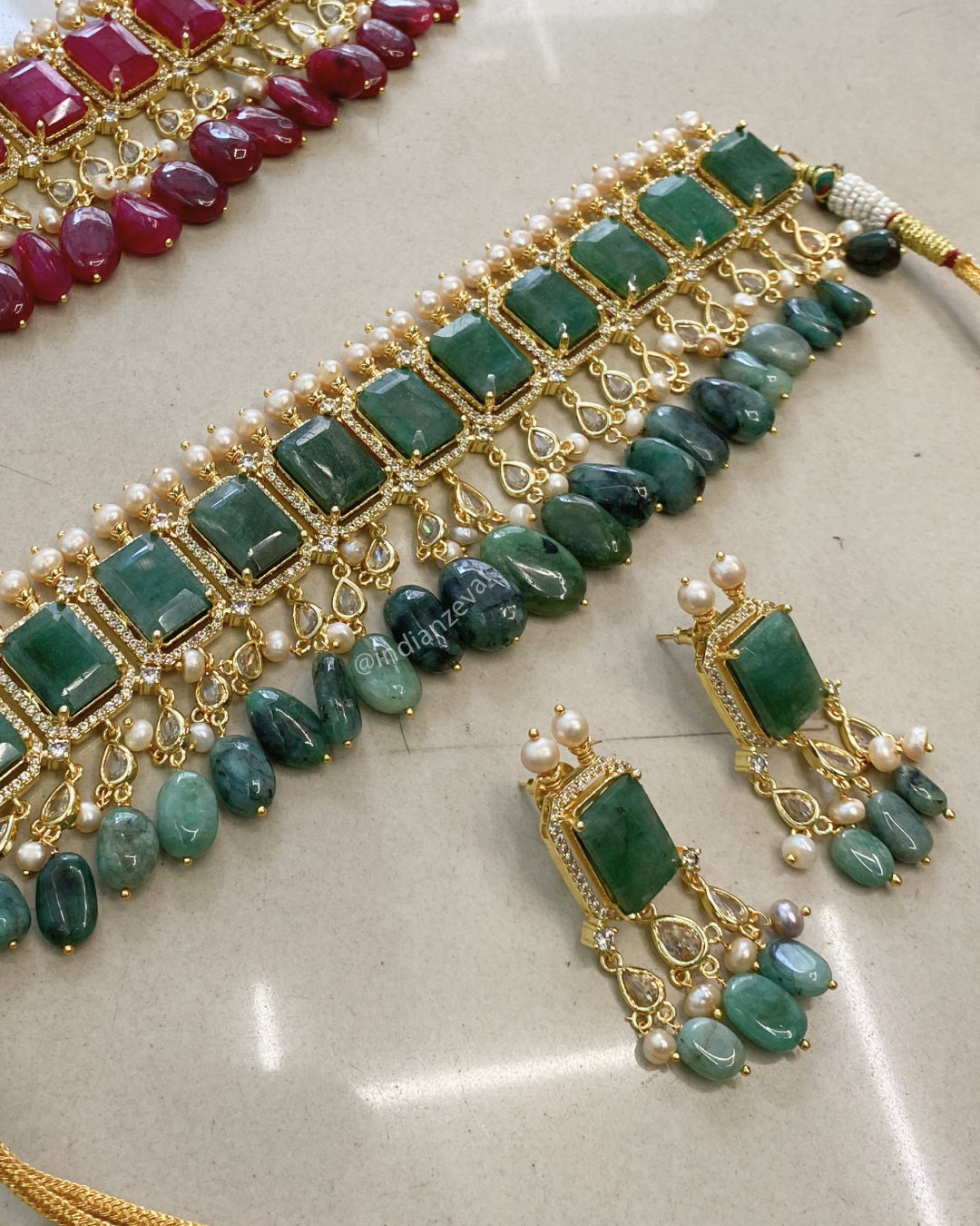 Jewelry set with green stones and gold accents on a light background. Luxury bridal emerald green choker necklace with antique pearls, CZ stones – Indian wedding jewelry Hyderabad, pearl jewelry for brides.