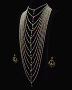 A multi-strand beaded necklace set displayed on a black mannequin bust against a black background, with matching dangling earrings shown at the sides. The necklace features many strands of small light beads with green and purple stone accents.