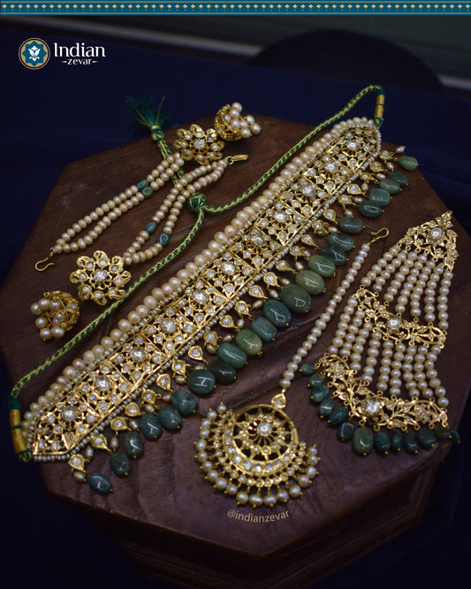 A close-up image of a Hyderabadi Jadau bridal choker set featuring antique pearls, Zambian emeralds, and intricate gold-plated alloy work. The set includes a choker, earrings, and a maang tika, zhumar adorned with Zambian emeralds.