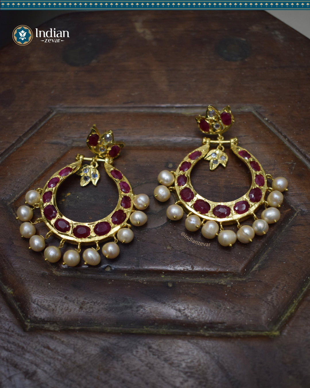 A close-up image of large Hyderabadi Jadau Chandbali earrings with freshwater pearls and rubies. The earrings feature intricate Jadau work and a gold-plated alloy base.