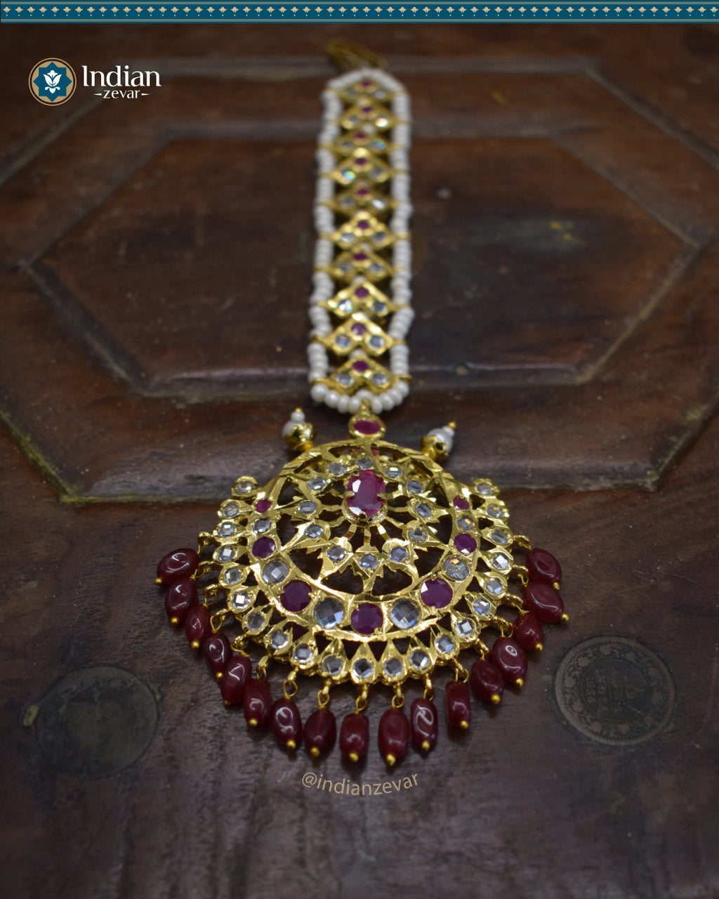 A close-up image of a Hyderabadi Jadau maang tika, adorned with dark pink and white CZ Polki stones and faux pearls. The maang tika is handcrafted with gold-plated alloy and features intricate Jadau work