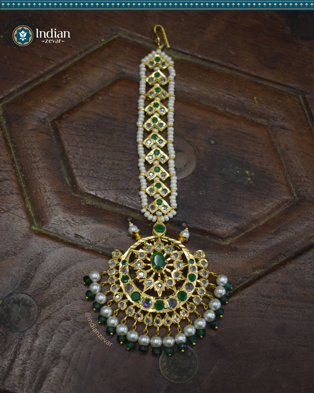 A close-up image of a Hyderabadi Jadau maang tika, adorned with green and white CZ Polki stones and faux pearls. The maang tika is handcrafted with gold-plated alloy and features intricate Jadau work.