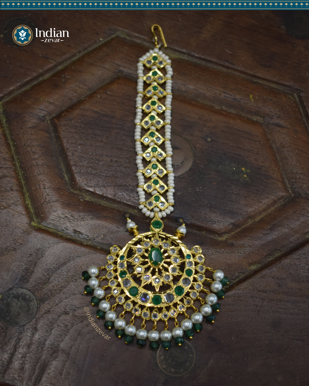 A close-up image of a Hyderabadi Jadau maang tika, adorned with green and white CZ Polki stones and faux pearls. The maang tika is handcrafted with gold-plated alloy and features intricate Jadau work.