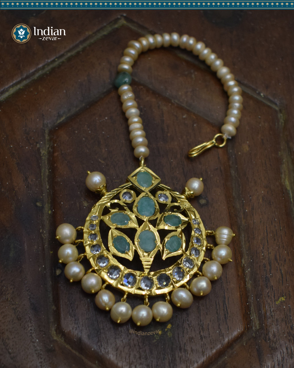 A close-up image of a Hyderabadi Jadau maang tika, adorned with emeralds, CZ Polki stones, and real freshwater pearls. The maang tika is handcrafted with gold-plated alloy and features intricate Jadau work.