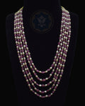 A multi-strand necklace displayed on a black mannequin bust against a black background. The necklace features alternating strands of faceted dusty rose ruby beads and cream-colored freshwater pearls, with a dark blue geometric logo printed on the center of the bust.