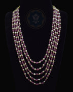 A multi-strand necklace displayed on a black mannequin bust against a black background. The necklace features alternating strands of faceted dusty rose ruby beads and cream-colored freshwater pearls, with a dark blue geometric logo printed on the center of the bust.