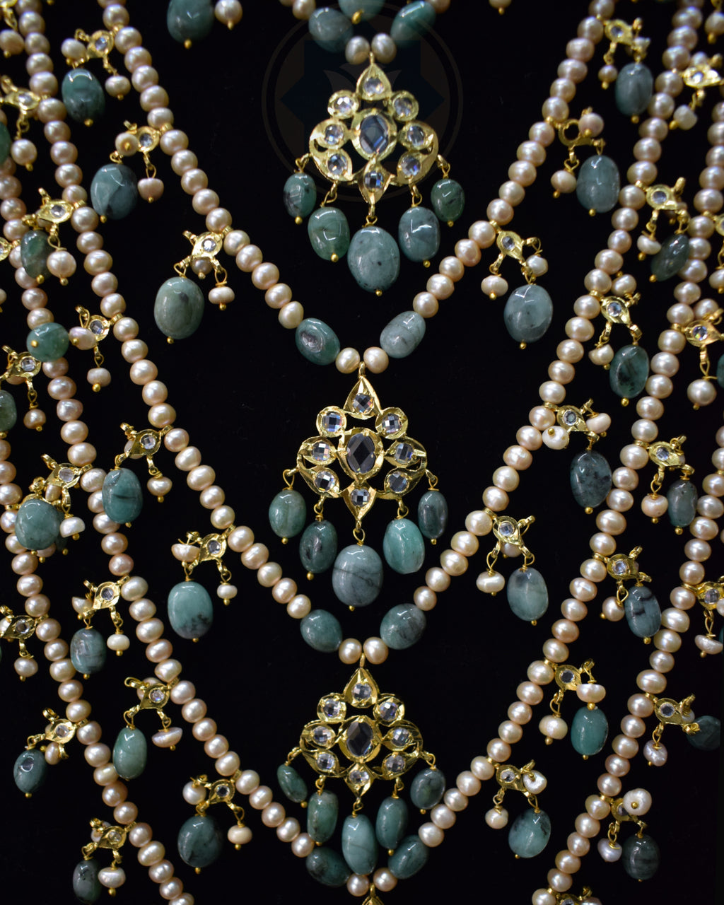 Closeup of Indian Zevar Grand Emerald Sathlada with seven strings of freshwater pearls, emerald Jadau hangings, CZ Polki and matching Angoor Goshe chandelier earrings.