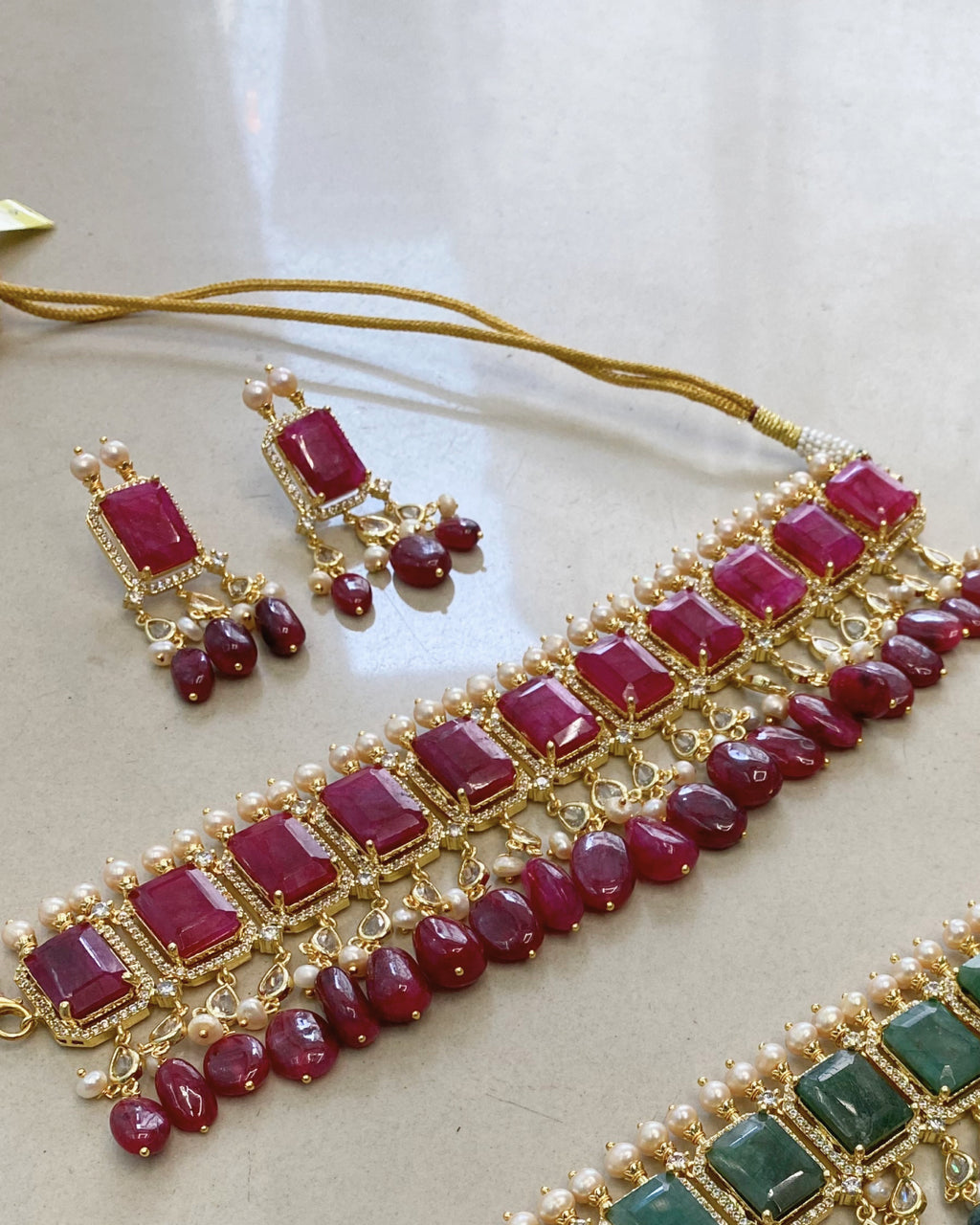Jewelry set with red gemstones and gold accents on a light background. Handcrafted Indo-Western choker set with pearls, emerald accents & Jadau work – perfect Indian bridal jewelry and wedding choker design.
