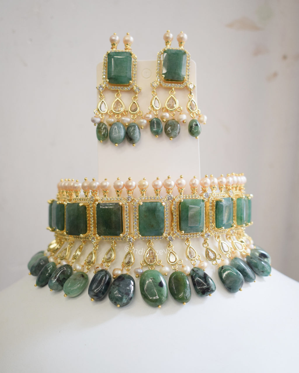 Green stone jewelry set on a mannequin with a white background. Indo-Western emerald green choker necklace set with pearls & CZ stones – Indian bridal jewelry, Hyderabadi pearl choker necklace online.