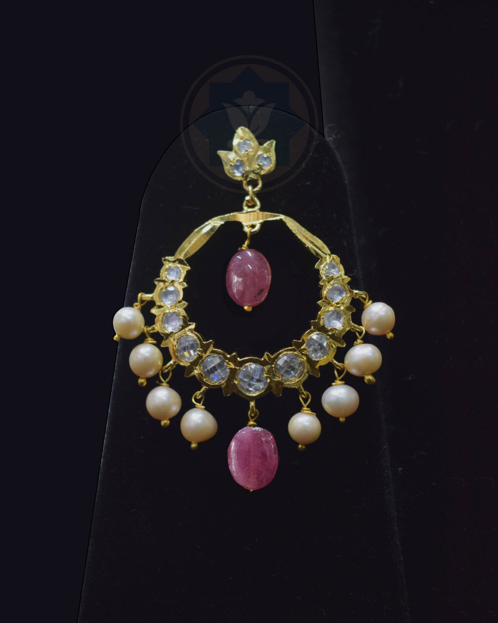 A gold crescent-shaped dangle earring decorated with clear crystals, white pearls, and pink gemstone accents, displayed on a black stand.