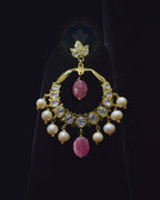 A gold crescent-shaped dangle earring decorated with clear crystals, white pearls, and pink gemstone accents, displayed on a black stand.