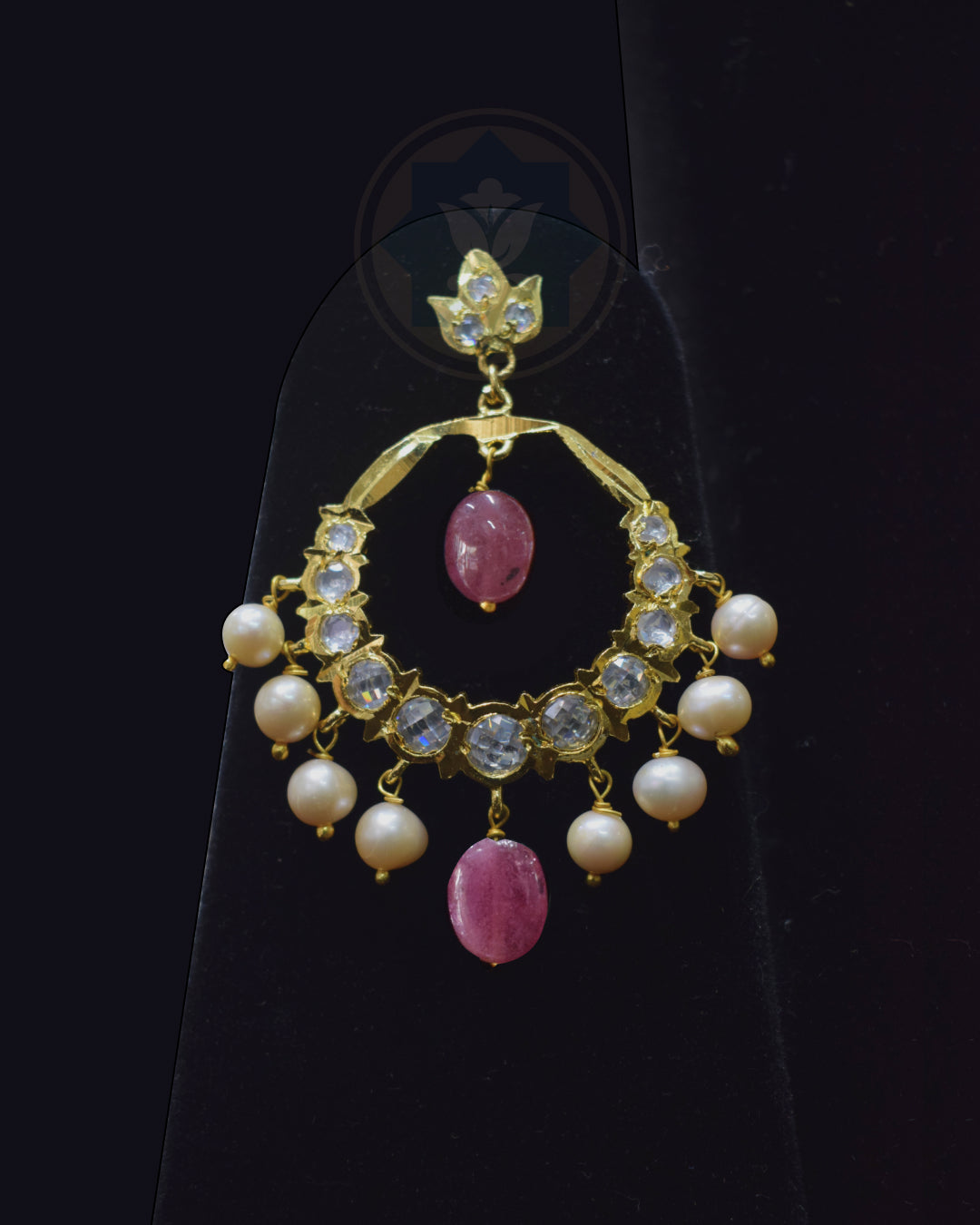 A gold crescent-shaped dangle earring decorated with clear crystals, white pearls, and pink gemstone accents, displayed on a black stand.