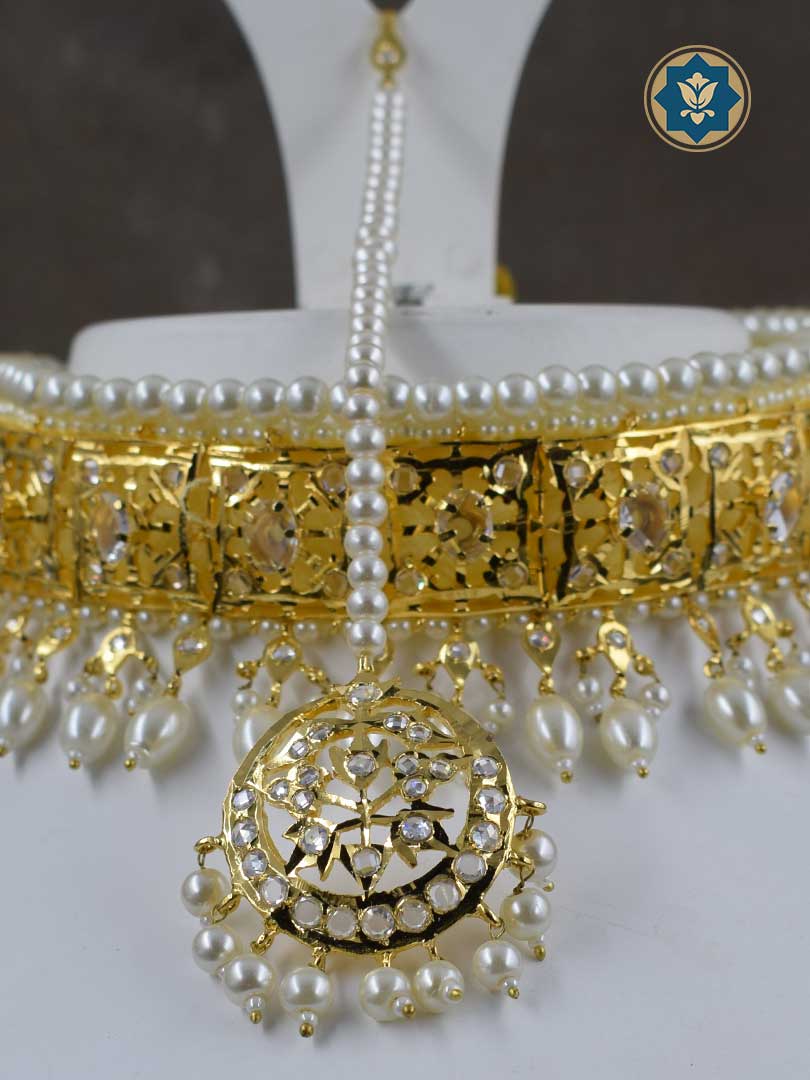 Achieve a traditional look with our Classic Hyderabadi Choker Set, including a Maang Tikka and Jhumka pair. Handmade with faux pearls and adorned with CZ polki stones, this set is plated with 6 carat gold for a luxurious appearance. Handmade in India with unique irregularities that enhance its beauty. Get ready to make a statement with this timeless piece