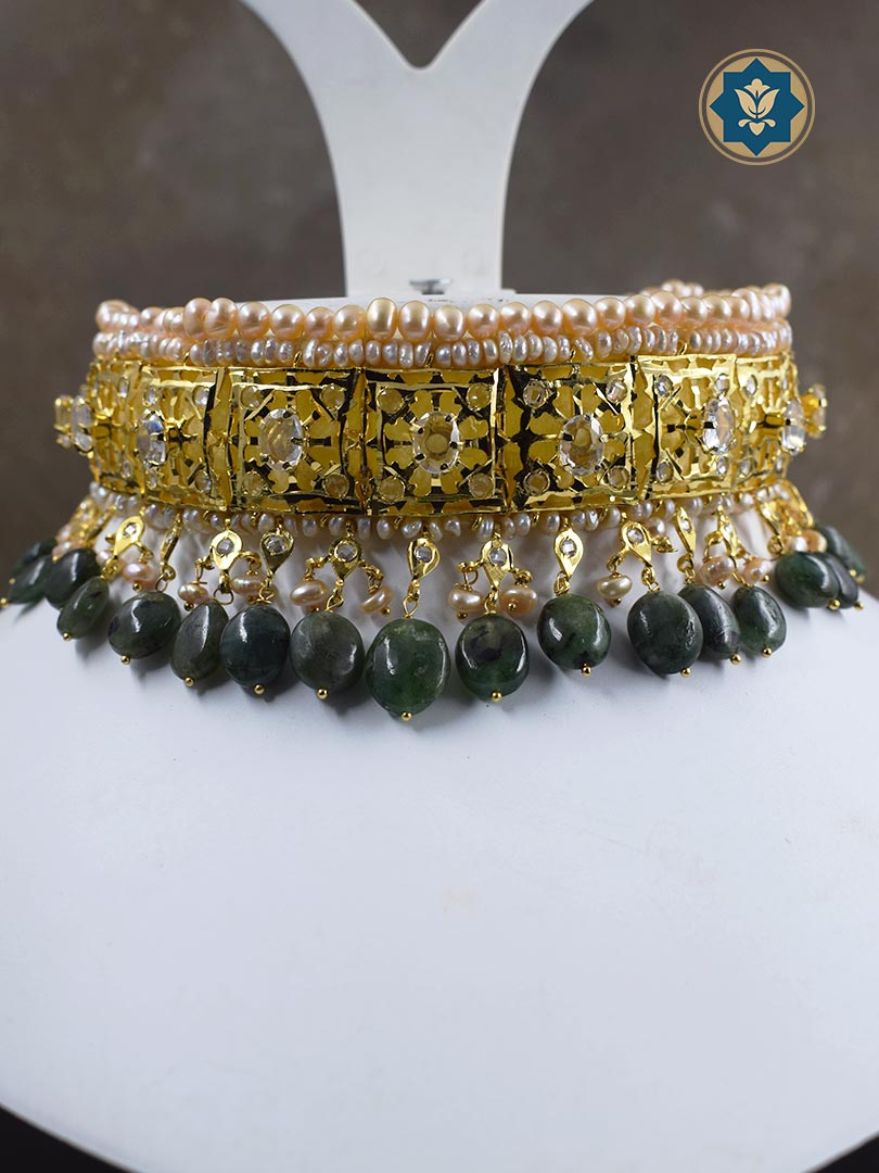 A classic Hyderabadi choker set featuring real freshwater old pearls and dark emeralds, handcrafted with 6 crt gold plating for a luxurious touch.