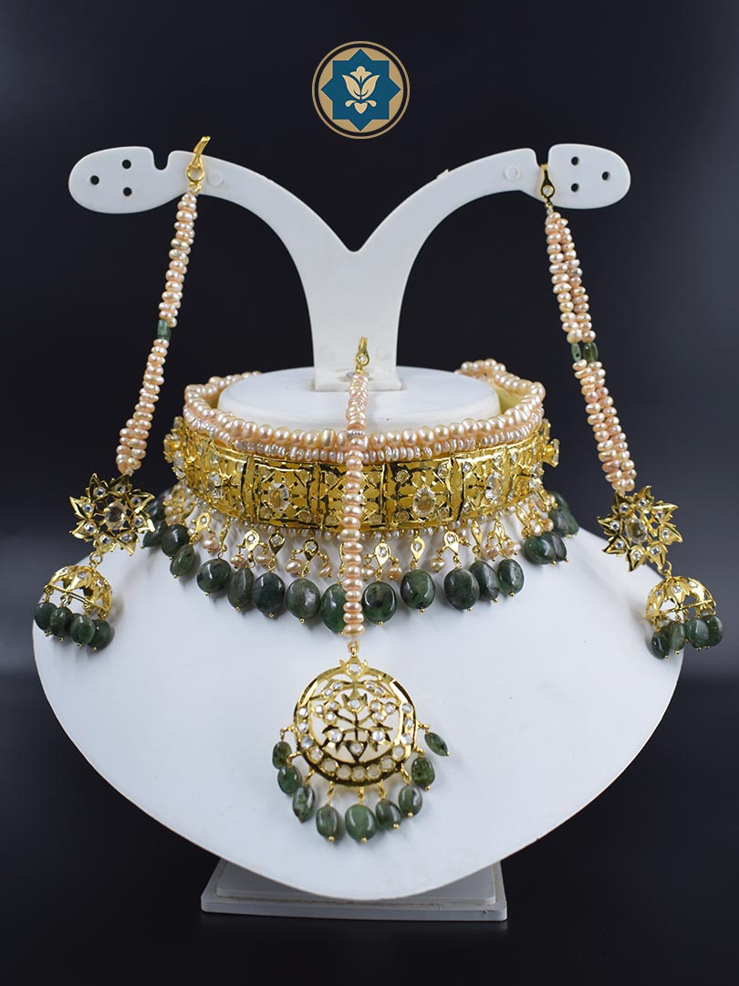 Handmade classic Hyderabadi choker set featuring real freshwater old pearls and dark emeralds. 6 carat gold plated Gulband Jadavi lachcha design with matching Maang Tikka and Jhumka earrings. Adorned with CZ polki stones. Made in India with unique irregularities that add to its natural beauty.